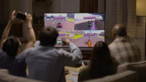 Four people on a couch playing a split-screen racing video game, cheering at the TV displaying "Finished!.