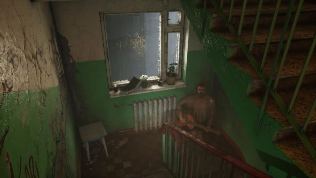 A man sits on a stairwell landing, playing guitar near a window in a worn, dimly lit building in Ebola Village.