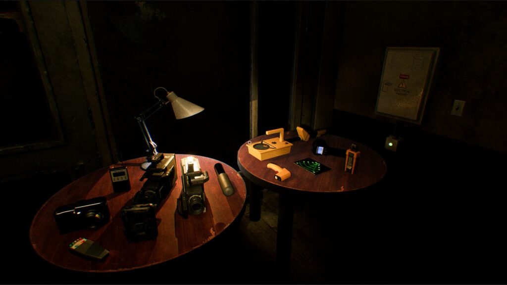 Two wooden tables in a dimly lit room, containing various items including cameras, a lamp, and electronic devices.