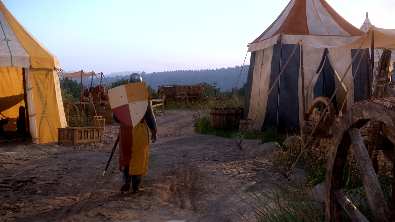 A knight with a shield walks near medieval tents and wooden carts on a dirt path at sunset.