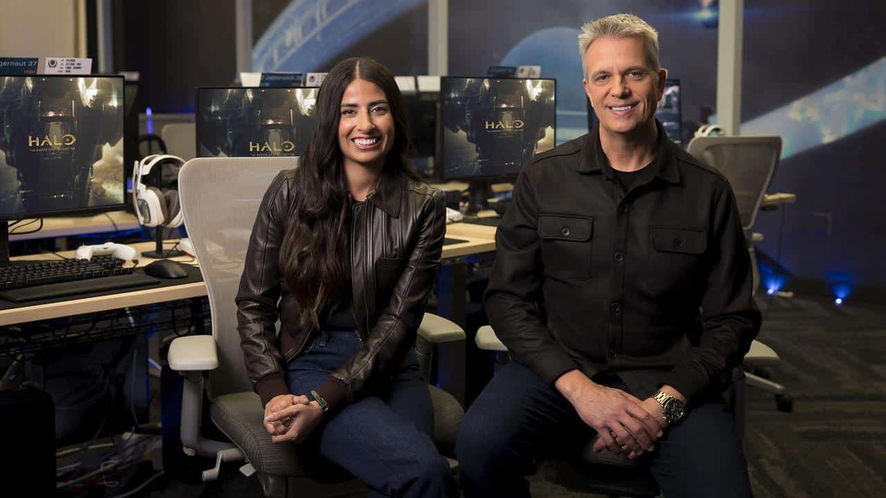Asha Sharma and Matt Booty sitting in a Halo playtest room with Xbox stations behind them.