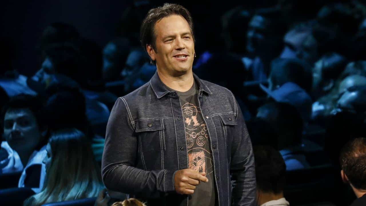 Phil Spencer speaking on stage during an Xbox presentation, with the audience in the background.