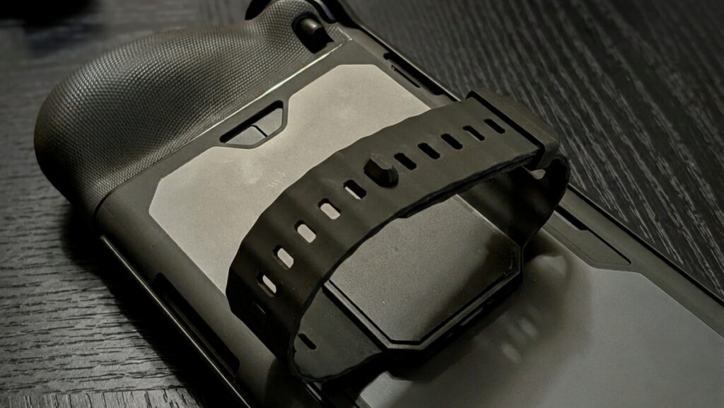 A close-up view of a gaming controller with a strap attached, resting on a dark wooden surface.
