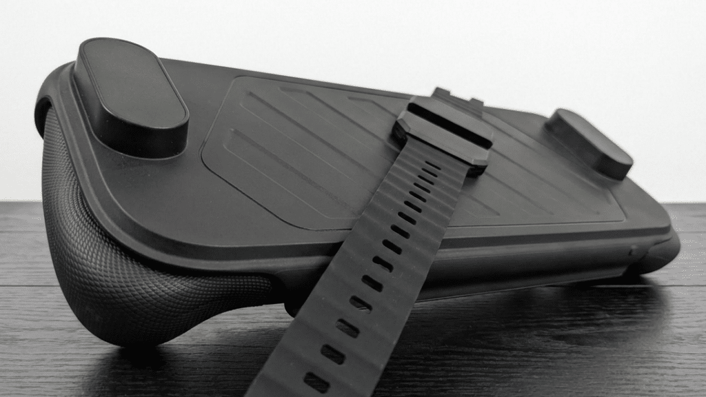 A close-up of a black game controller grip with an adjustable strap on a dark wooden surface.
