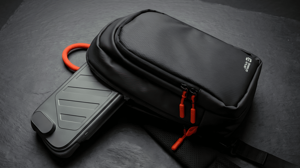 A sleek black backpack with orange zippers and a side pocket, featuring a portable charger resting beside it on a textured surface.