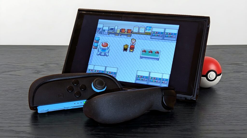 A Nintendo Switch with controllers displays a Pokémon game, with a Poké Ball in the background on a black table.
