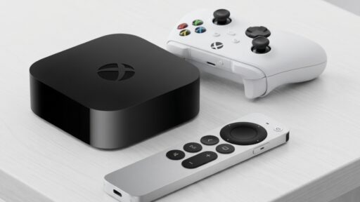 A black Xbox streaming device, a white Xbox controller, and a silver remote on a white surface.