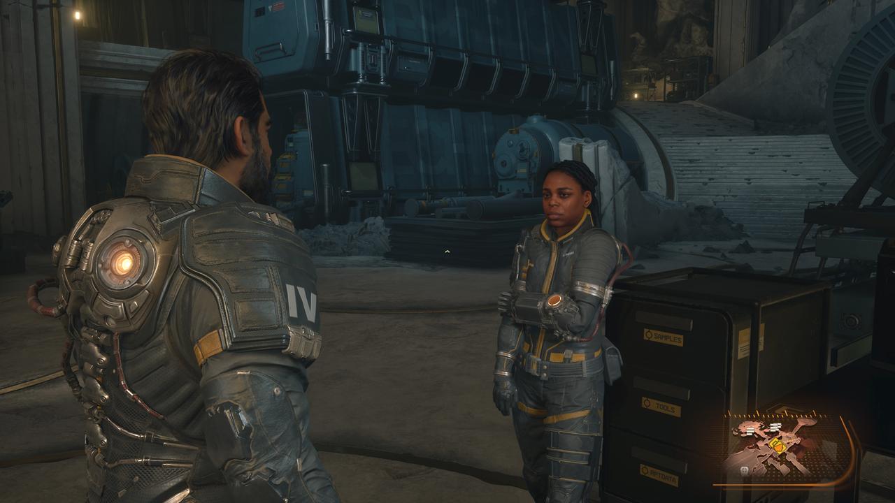 Arjun Devraj, wearing his enforcer suit, talks to a member of the Echelon IV crew within the industrial hub of The Passage.
