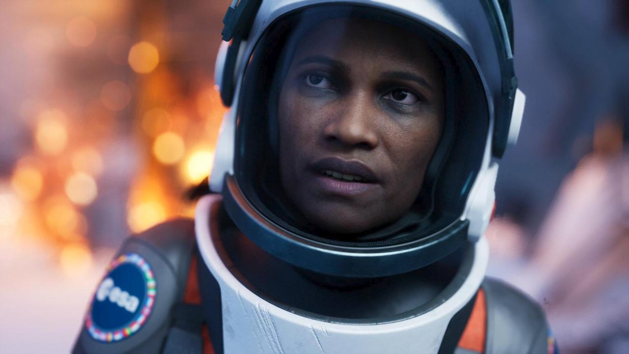 A close-up of astronaut Ariane Montclair looking worried inside her space helmet after the Hope-01 escape pod crash in Aphelion. An ESA patch is clearly visible on her shoulder.