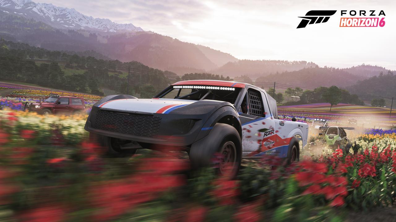 An off-road racing truck driving through a vibrant field of red and yellow flowers toward mountains in Forza Horizon 6.