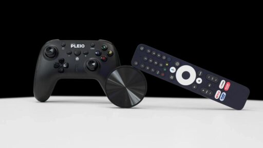 A black PLEIO gamepad sitting next to a circular Netgem streaming device and a remote control on a white surface.