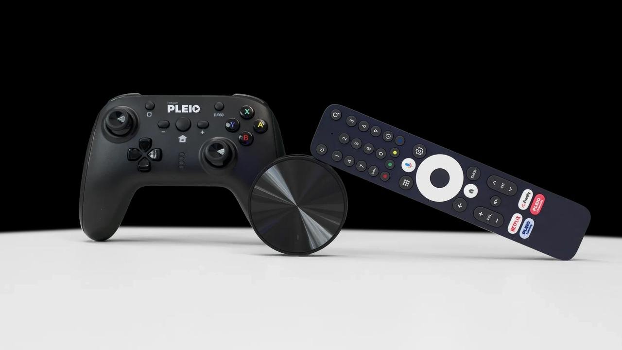 A black PLEIO gamepad sitting next to a circular Netgem streaming device and a remote control on a white surface.
