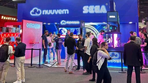 A wide view of Nuuvem’s massive blue two-story exhibition booth at Gamescom Latam. The booth features glowing Nuuvem and SEGA logos, with crowds of people engaging at gaming stations. A red pillar on the left displays the CriticalLeap publishing label.
