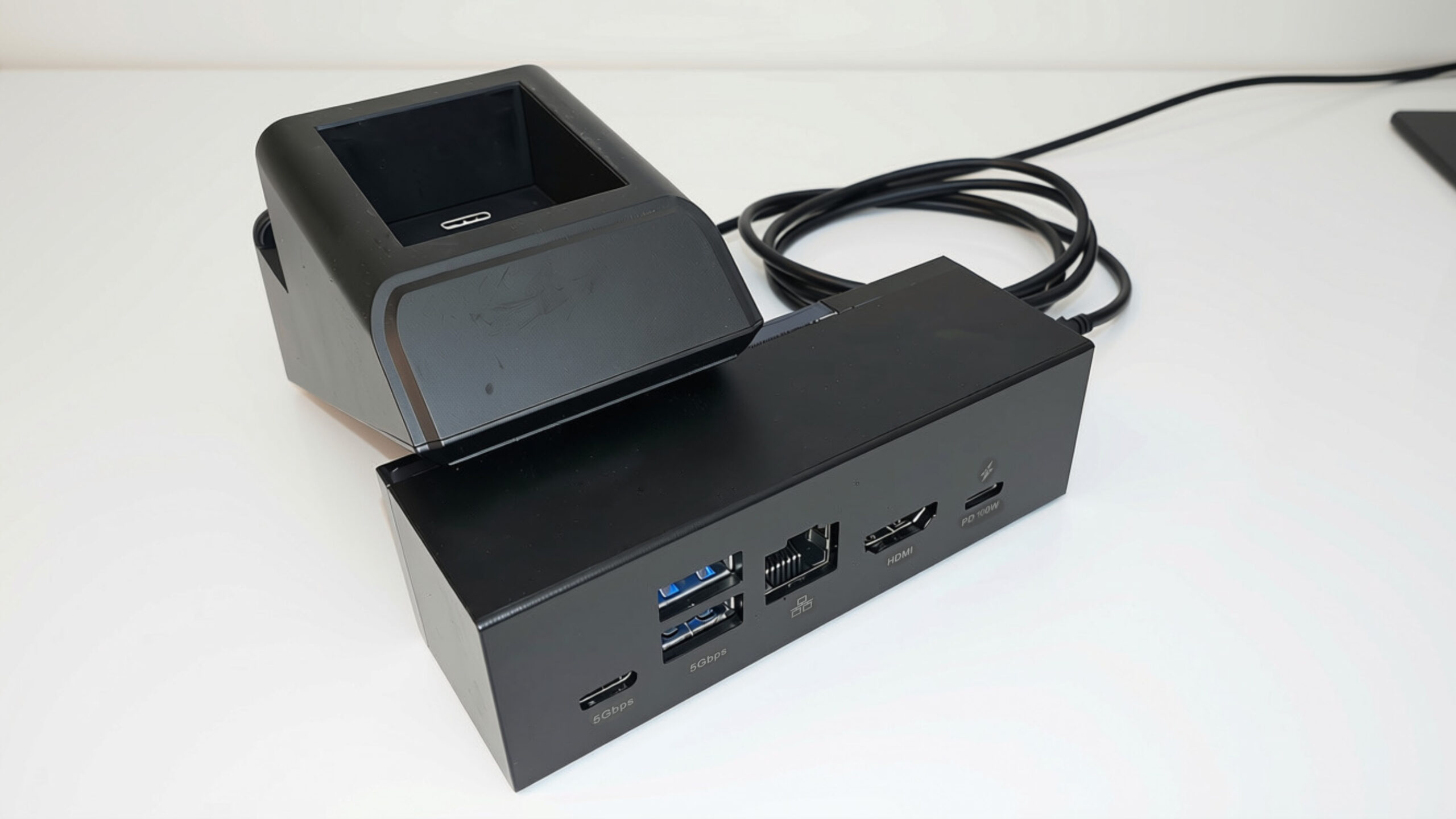 Disseny sense títol - 1 Black docking station with USB, Ethernet, HDMI, and 5Gbps ports beside a charging stand