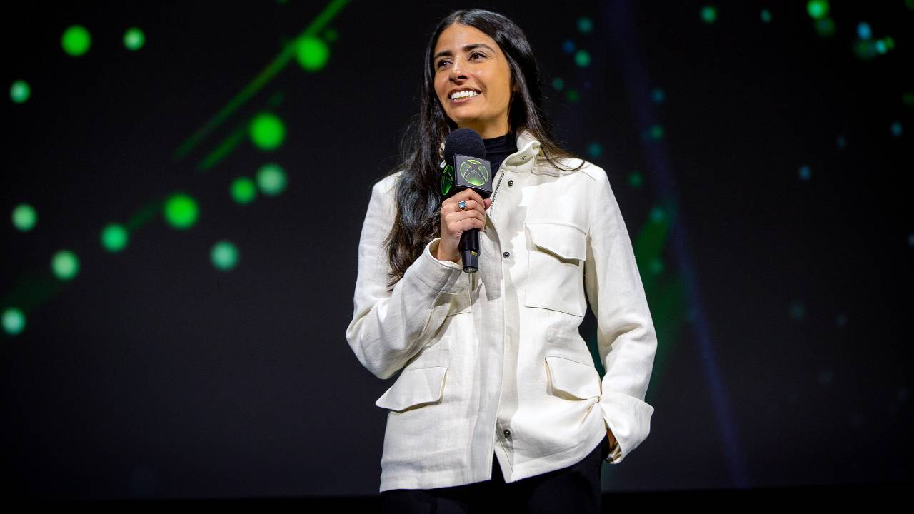 XBOX executive Asha Sharma speaking on stage with an XBOX-branded microphone.