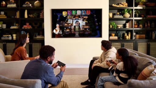 Four people gathered in a living room playing a digital board game on a Samsung TV, with smartphones used as controllers.